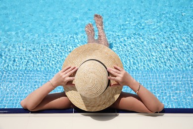 Woman with straw hat resting in outdoor swimming pool on sunny day, above view