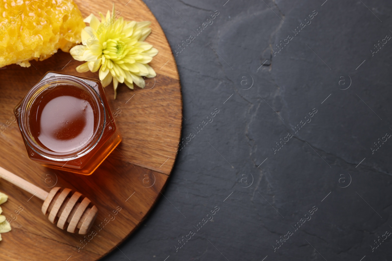 Photo of Sweet honey in jar, dipper, chrysanthemum flowers and pieces of honeycomb on grey textured table, top view. Space for text