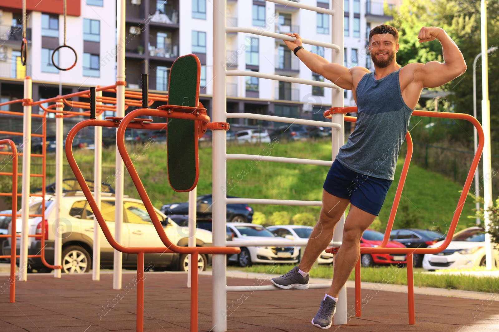 Photo of Smiling man showing biceps at street gym on sunny day