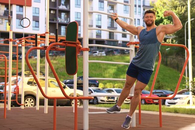 Photo of Smiling man showing biceps at street gym on sunny day