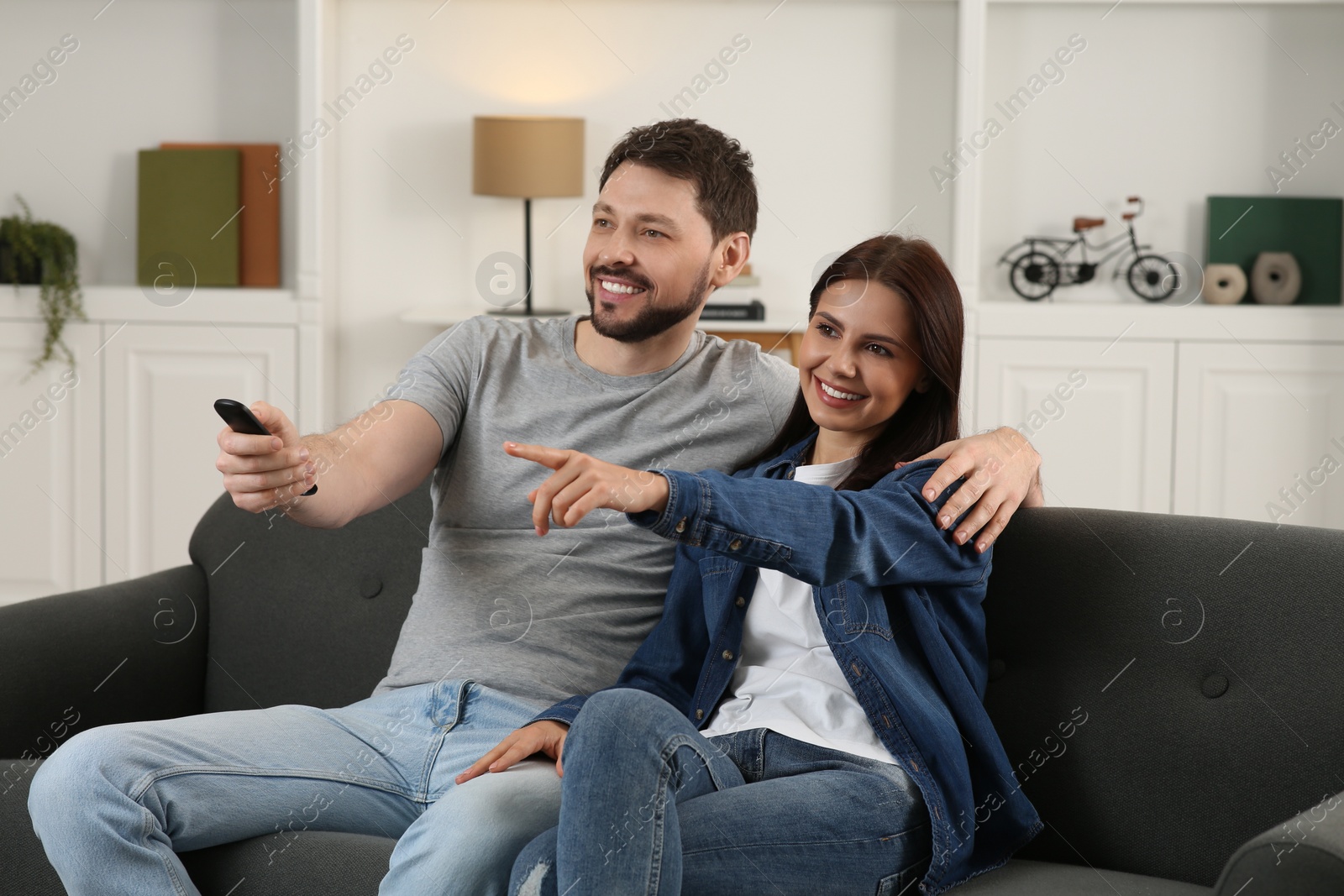 Photo of Happy couple watching show at home. Man changing TV channels with remote control