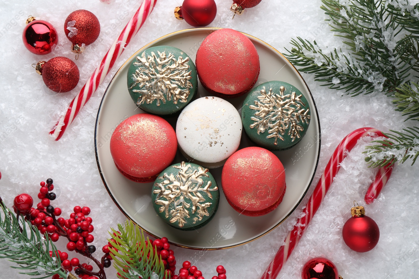 Photo of Beautifully decorated Christmas macarons, candy canes and festive decor on snow, flat lay