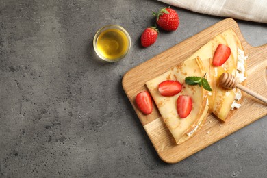 Delicious thin pancakes with strawberries, cottage cheese and honey on grey table, flat lay. Space for text