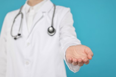 Doctor with stethoscope holding something on light blue background, closeup