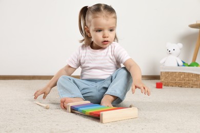 Photo of Cute little girl with xylophone and drumsticks at home