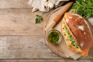 Delicious homemade garlic bread with herbs on wooden table, flat lay. Space for text