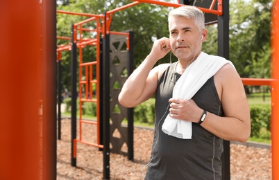 Handsome mature man listening to music on sports ground, space for text. Healthy lifestyle