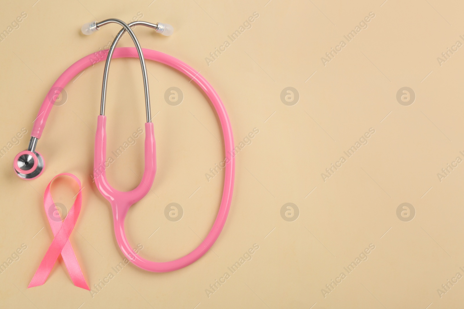 Photo of Pink ribbon and stethoscope on beige background, flat lay with space for text. Breast cancer concept