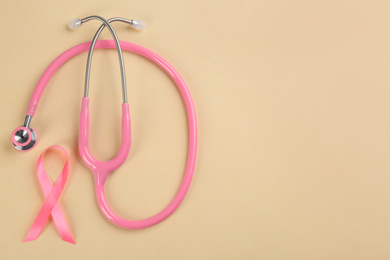 Photo of Pink ribbon and stethoscope on beige background, flat lay with space for text. Breast cancer concept