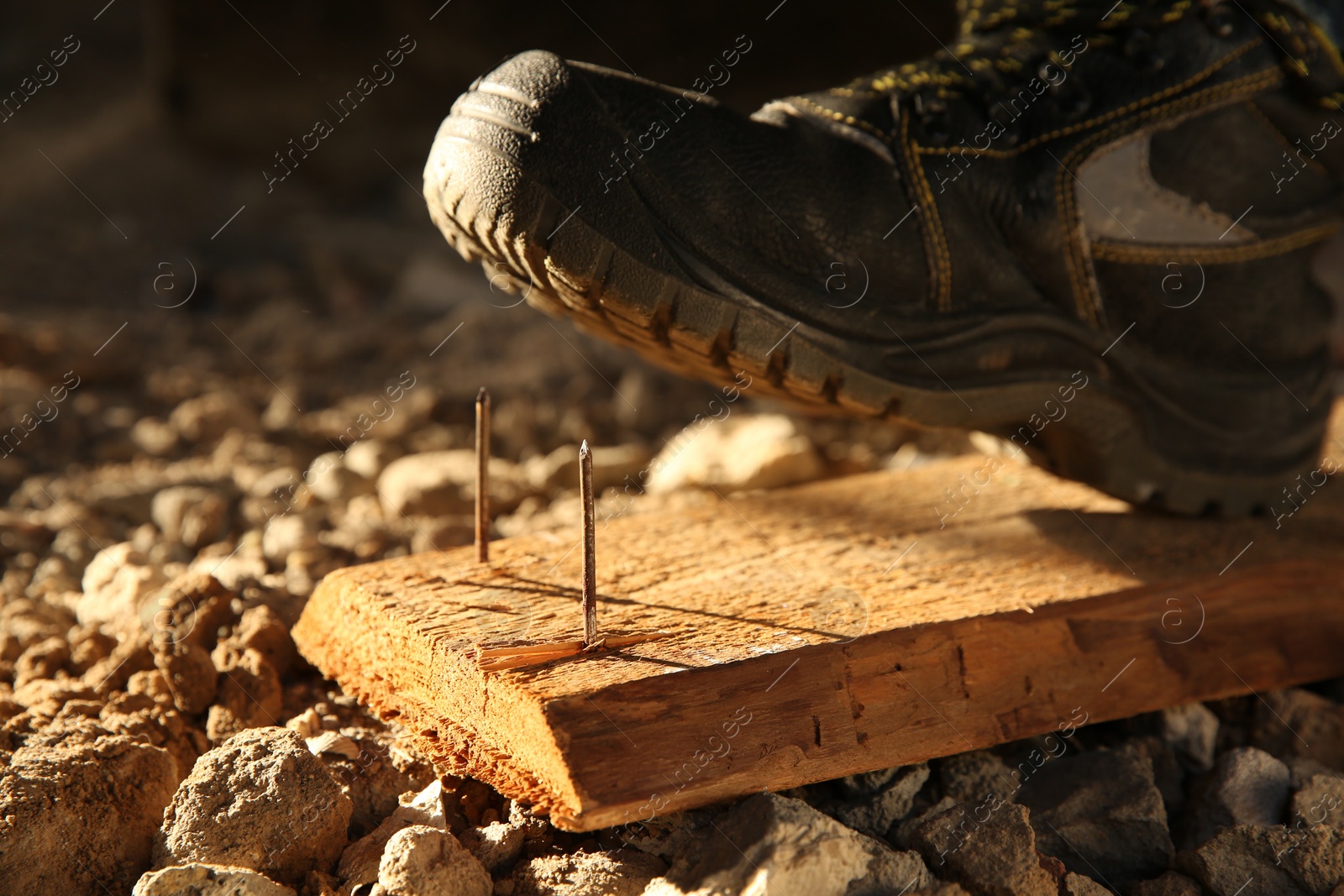 Photo of Careless worker stepping on nails in wooden plank, closeup