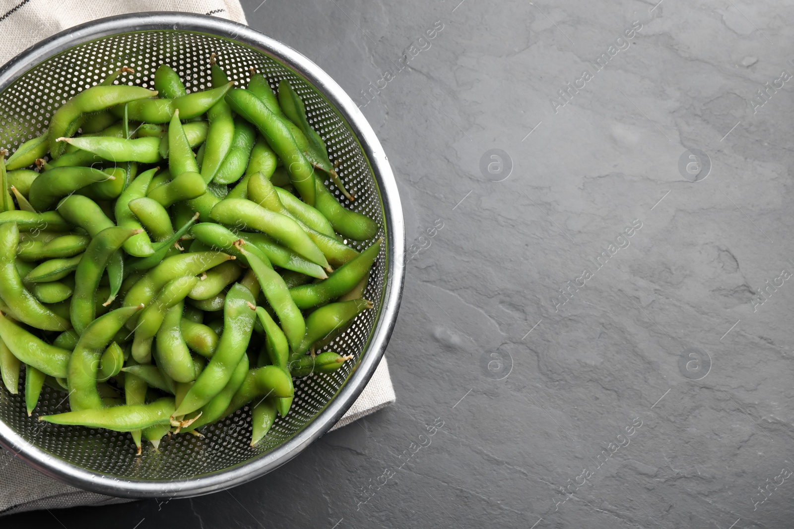 Photo of Sieve with green edamame beans in pods on black table, top view. Space for text