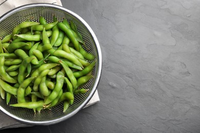 Sieve with green edamame beans in pods on black table, top view. Space for text