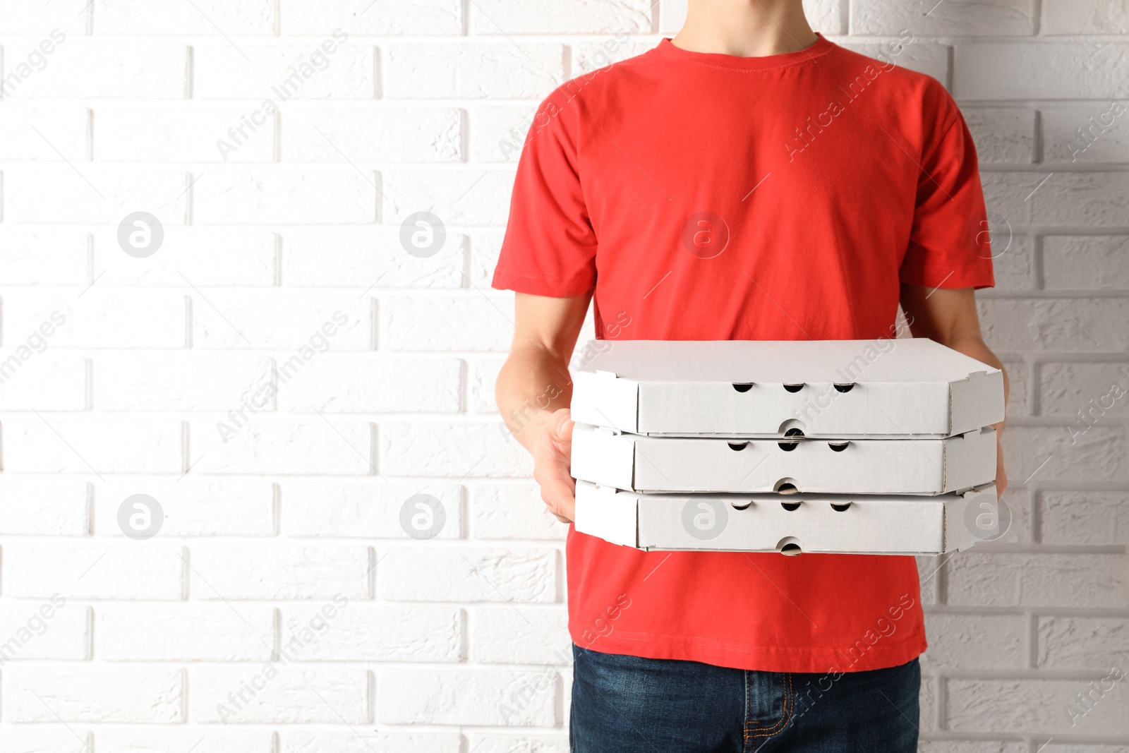 Photo of Young man with pizza boxes near white brick wall, space for text. Food delivery service