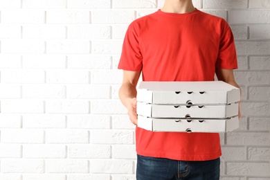 Photo of Young man with pizza boxes near white brick wall, space for text. Food delivery service