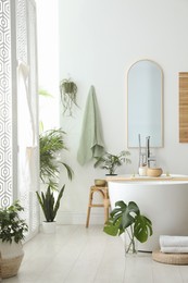 Photo of Stylish bathroom interior with modern tub, houseplants and beautiful decor. Home design