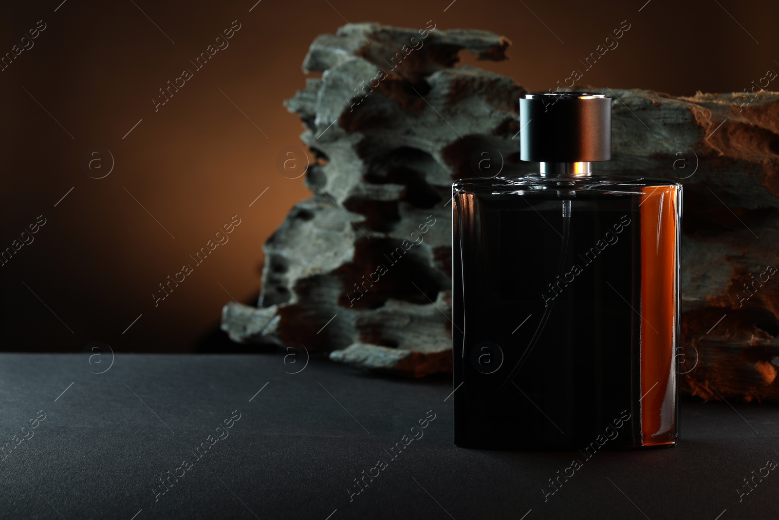 Photo of Luxury men`s perfume in bottle on grey table against brown background, space for text