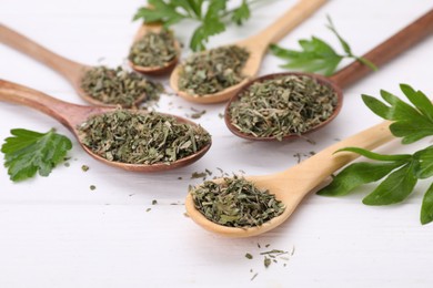 Photo of Spoons with dried aromatic parsley and fresh leaves on white wooden table, closeup