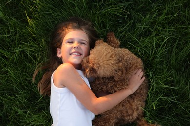 Beautiful girl with cute Maltipoo dog on green lawn outdoors, top view