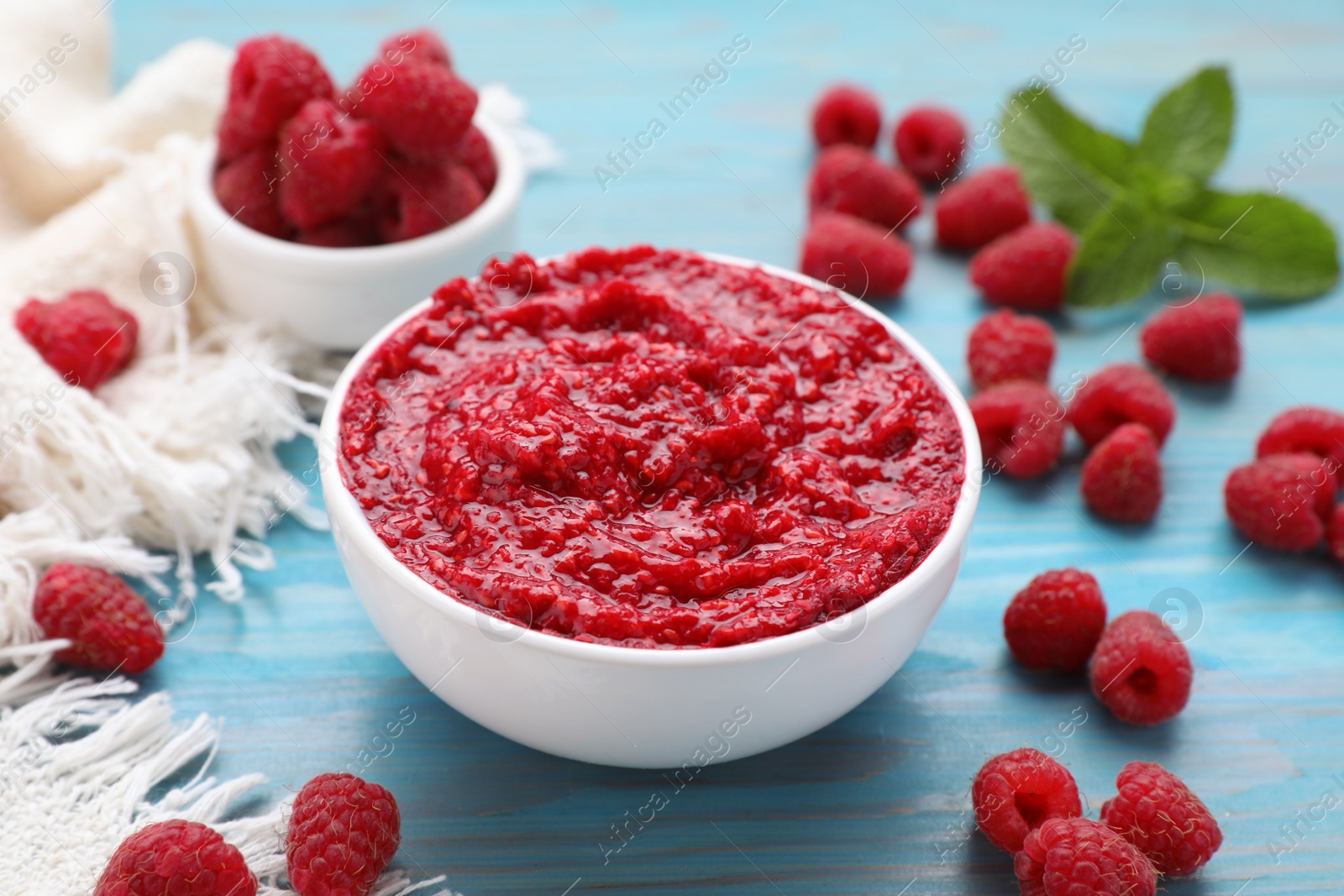 Photo of Raspberry puree in bowl and fresh berries on light blue wooden table