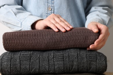 Photo of Woman with folded sweaters on light background, closeup