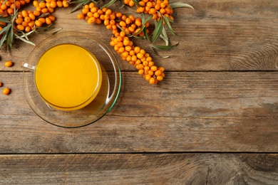 Photo of Sea buckthorn tea and fresh berries on wooden table, flat lay. Space for text