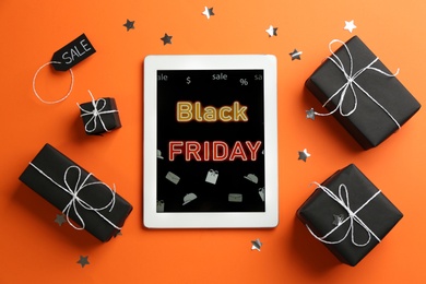 Photo of Tablet with Black Friday announcement and gifts on orange background, flat lay