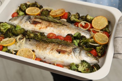 Woman holding baking dish with delicious fish and vegetables indoors, selective focus