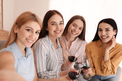 Photo of Beautiful young ladies with wine taking selfie indoors. Women's Day