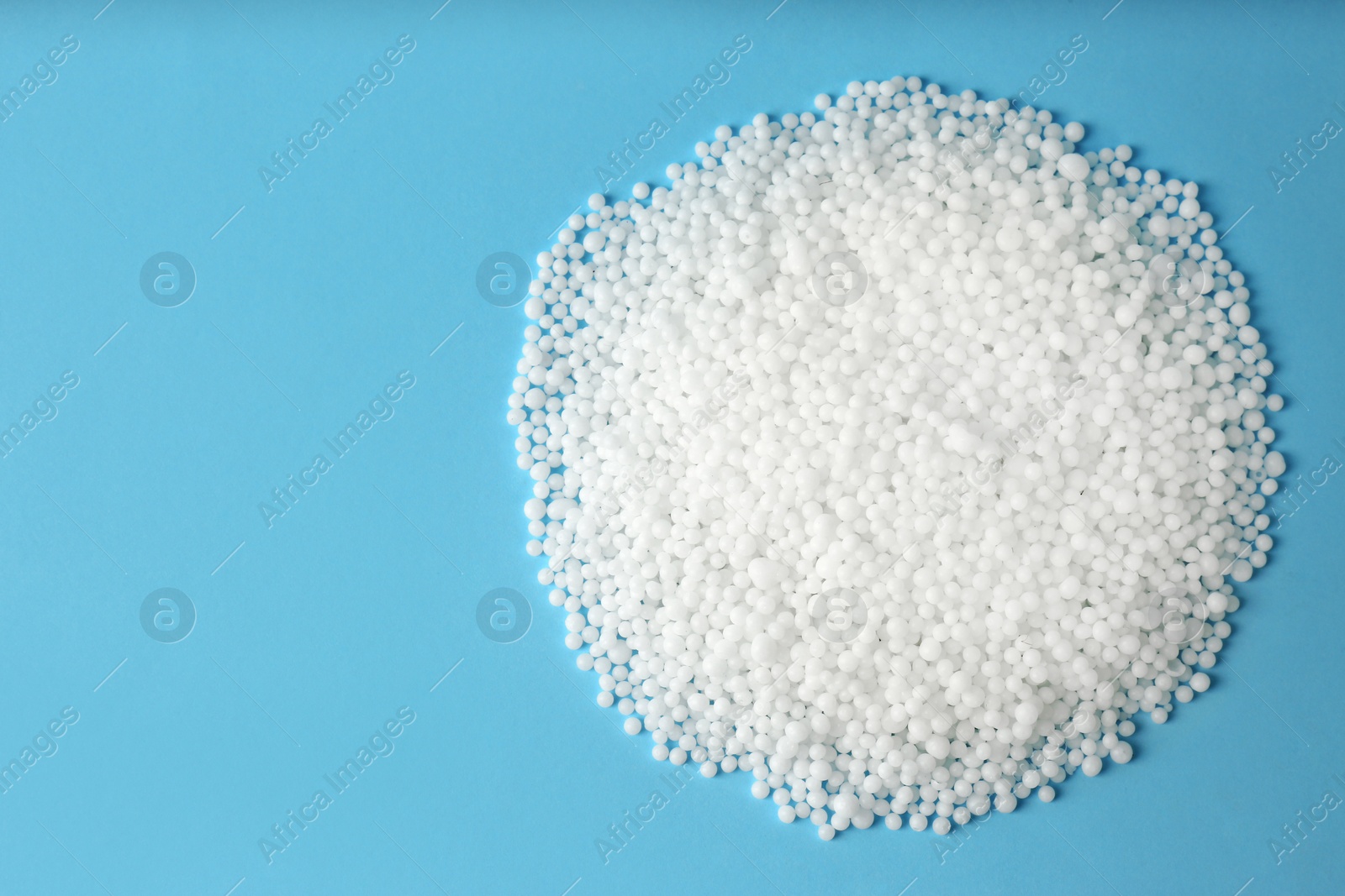 Photo of Pellets of ammonium nitrate on light blue background, flat lay with space for text. Mineral fertilizer