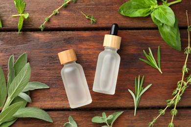 Photo of Bottles of essential oils and fresh herbs on wooden table, flat lay