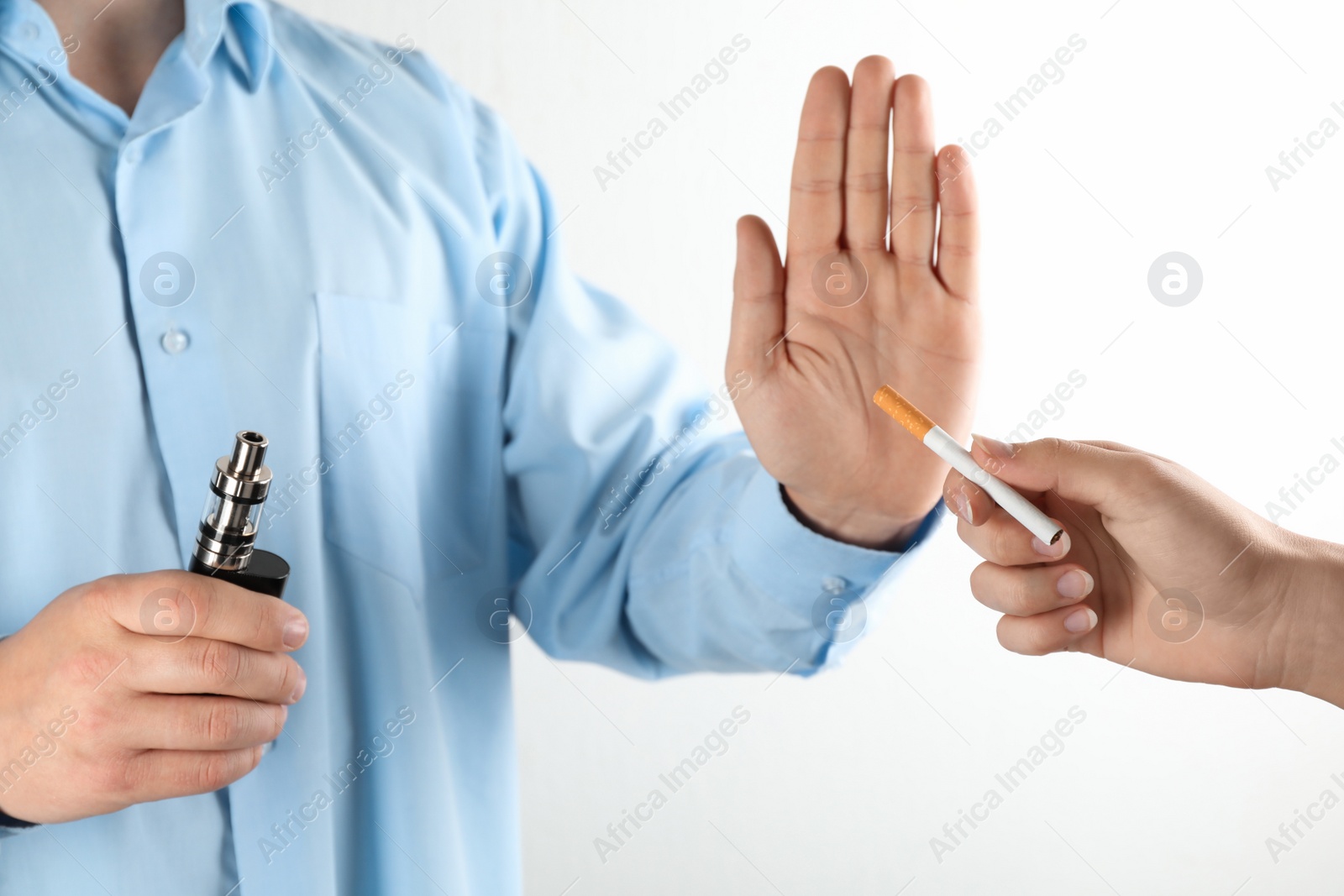 Photo of Man with vaping device refusing cigarette on light background, closeup. Smoking alternative