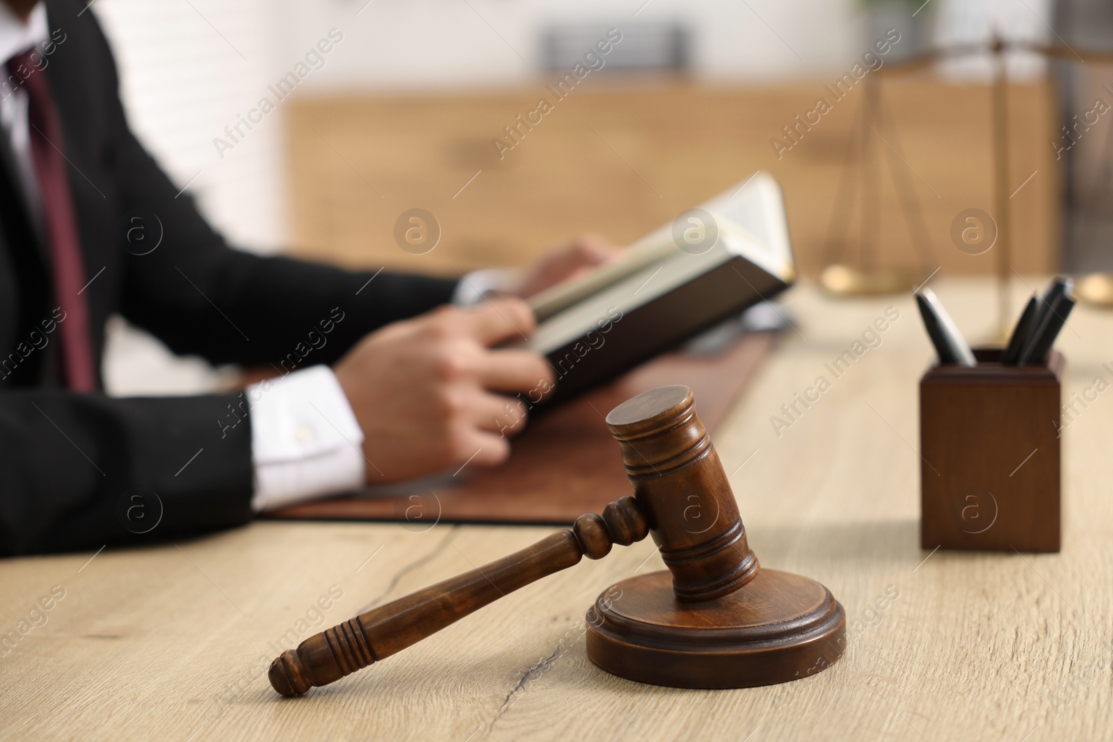 Photo of Lawyer reading book at table in office, focus on gavel