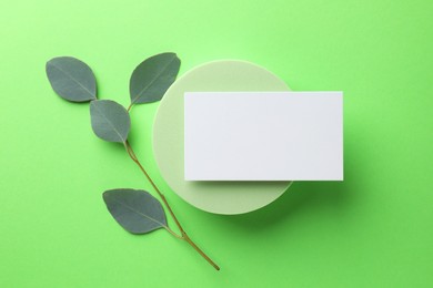 Empty business card, round podium and eucalyptus branch on light green background, top view. Mockup for design
