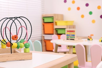 Photo of Toy bead maze on wooden table in playroom, space for text. Kindergarten interior design
