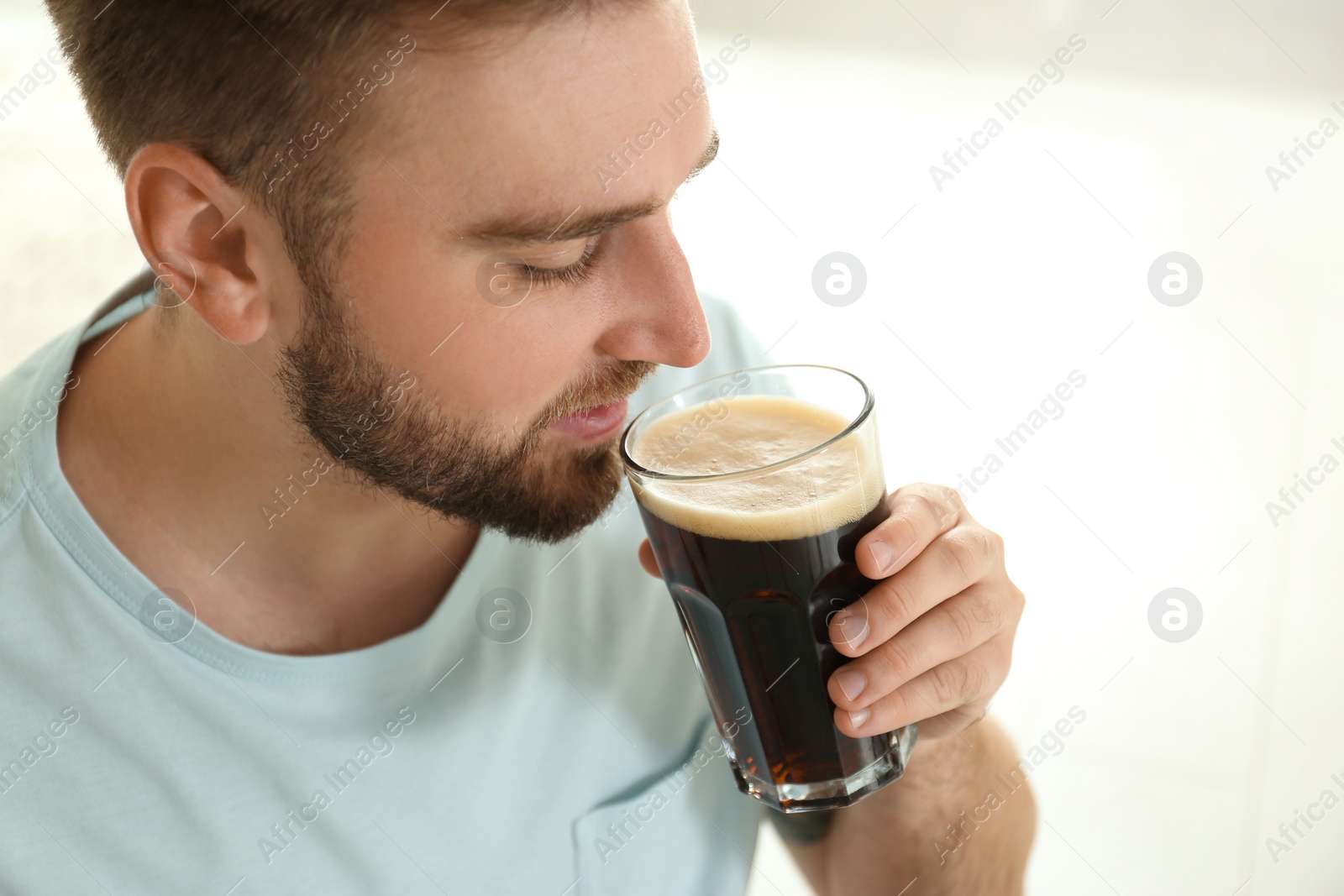 Photo of Handsome man with cold kvass indoors, closeup. Traditional Russian summer drink