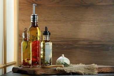 Cooking oil with different spices and herbs in bottles on wooden table. Space for text