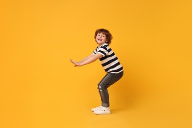 Happy little boy dancing on yellow background. Space for text
