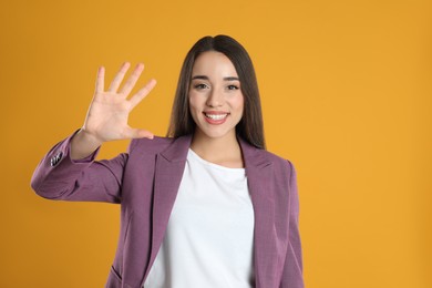 Photo of Woman in violet blazer showing number five with her hand on yellow background