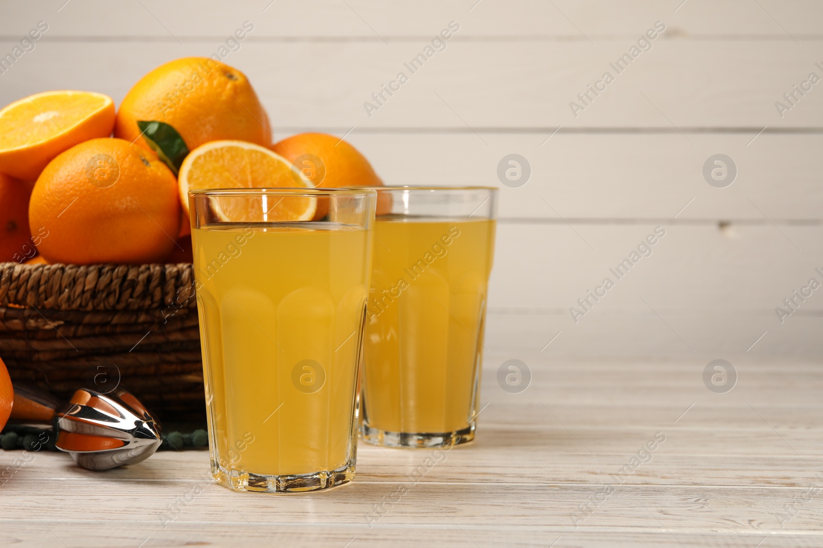 Photo of Many ripe juicy oranges, squeezer and fresh juice on white wooden table. Space for text