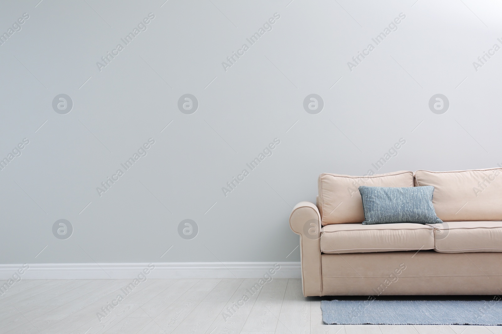 Photo of Comfortable beige sofa near light wall indoors, space for text. Simple interior