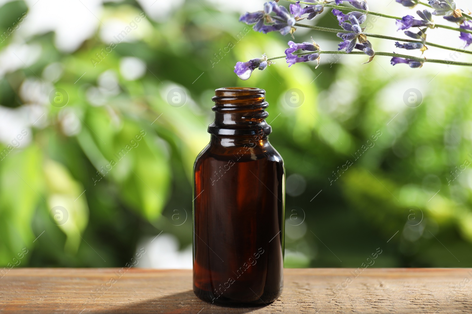 Photo of Bottle of lavender essential oil on wooden table against blurred background
