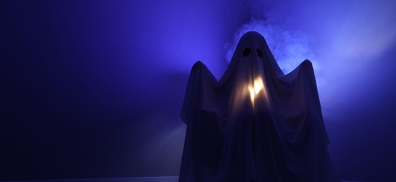 Creepy ghost. Woman covered with sheet in blue light, space for text