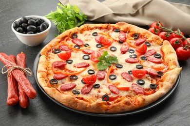 Tasty pizza with dry smoked sausages, olives, tomatoes, pepper and parsley on grey table