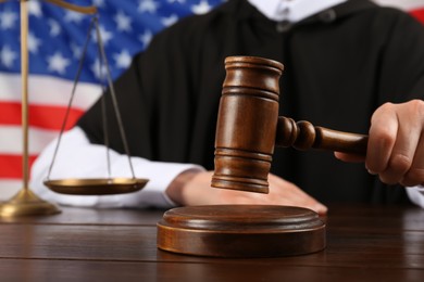 Photo of Judge with gavel at wooden table against flag of United States, closeup