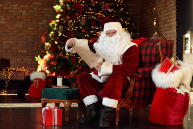 Santa Claus with wish list near Christmas tree indoors