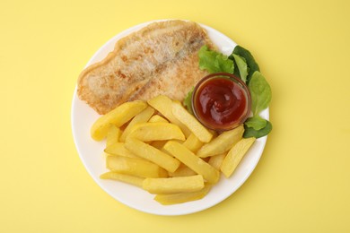 Photo of Delicious fish and chips with ketchup, spinach and lettuce on yellow table, top view
