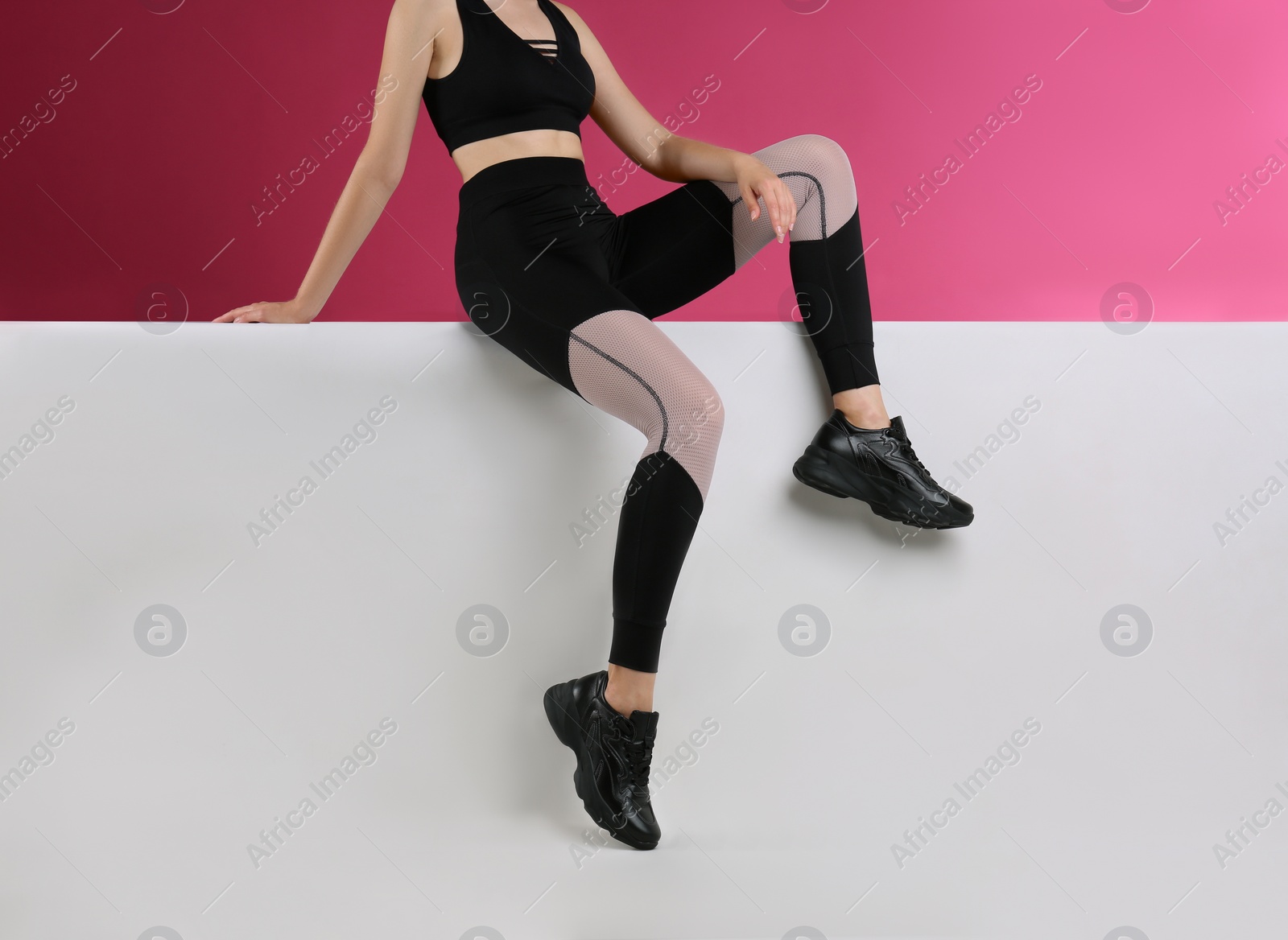 Photo of Woman in stylish sneakers sitting on color background, closeup