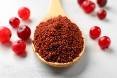 Photo of Dried cranberry powder in spoon and fresh berries on white table, closeup