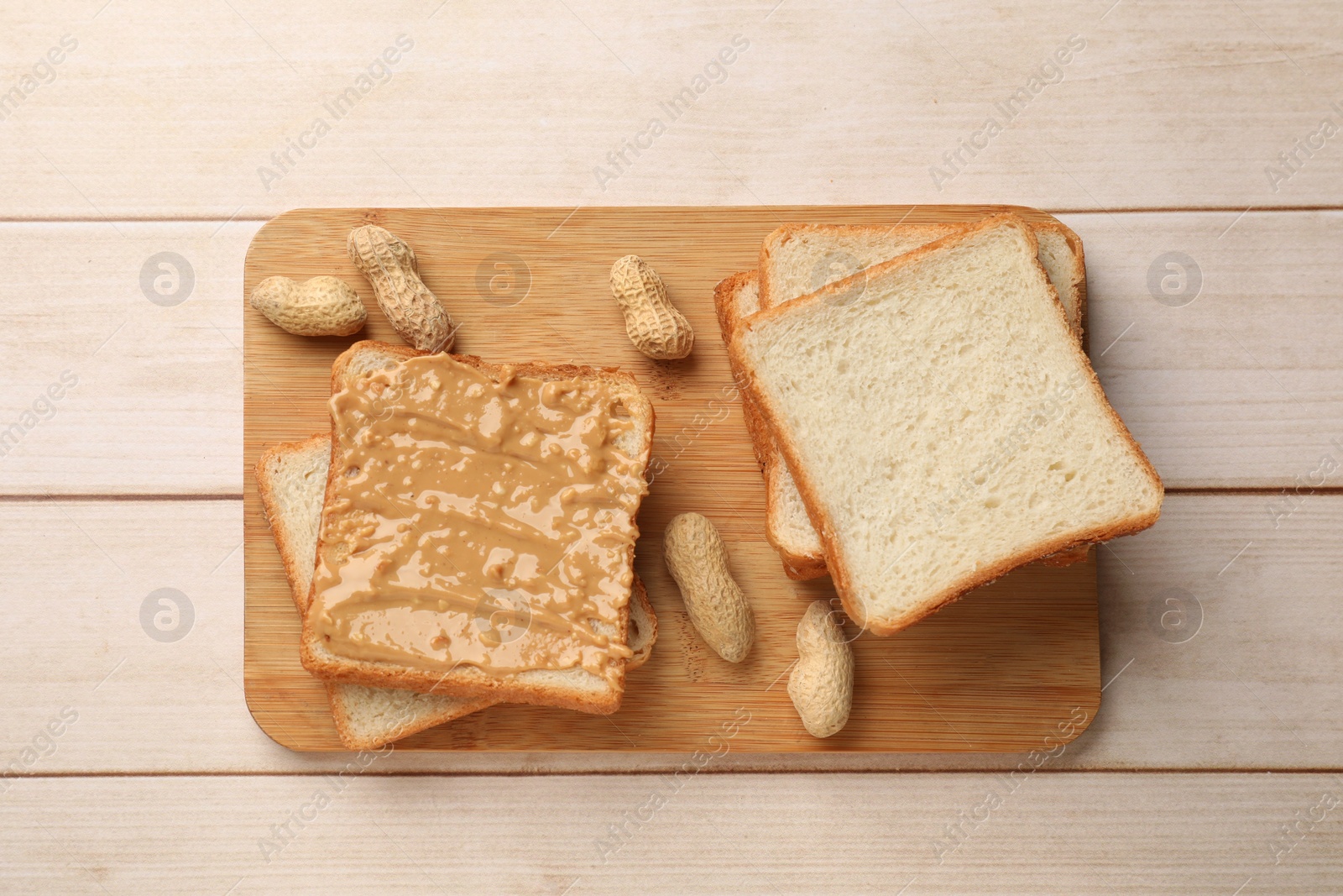 Photo of Delicious toasts with peanut butter and nuts on light wooden table, top view