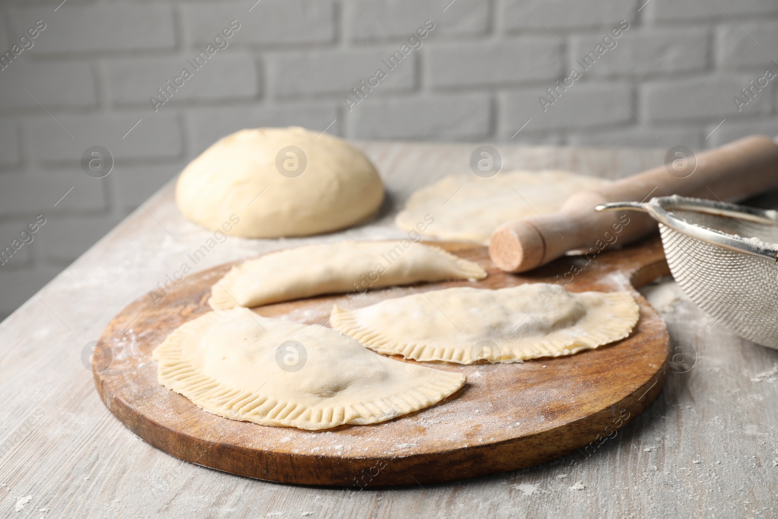 Photo of Raw chebureki with tasty filling and rolling pin on wooden table